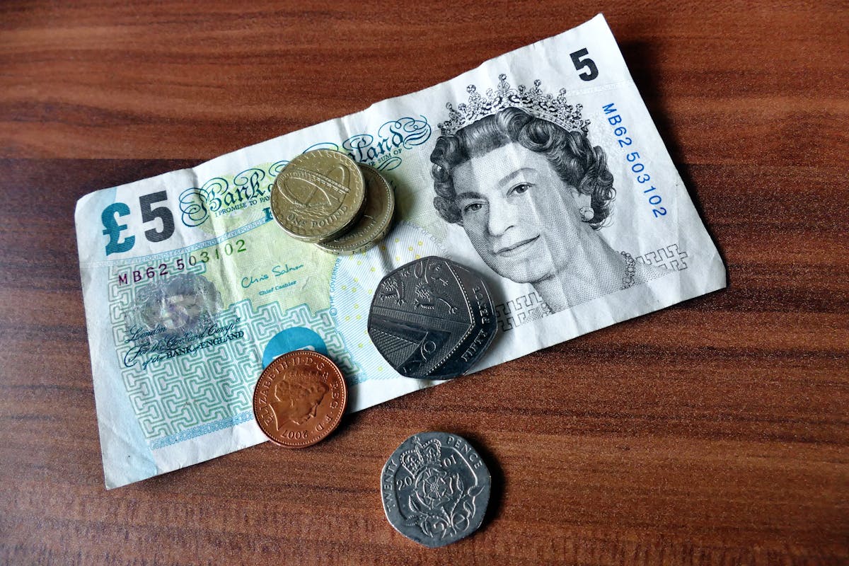 Billete de cinco libras y monedas británicas sobre superficie de madera